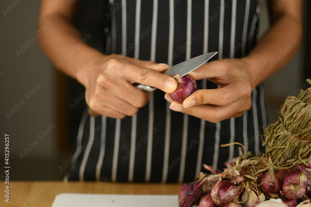 Obraz premium hands of a person with red onion peeling on white board in the kitchen
