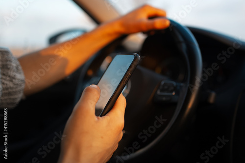 Close-up of male hands driving the car with smartphone in hand.