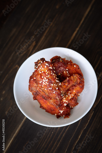 Chunks of fried chicken in a spicy sauce and sesame seeds. Food Korean cuisine on a wooden background.