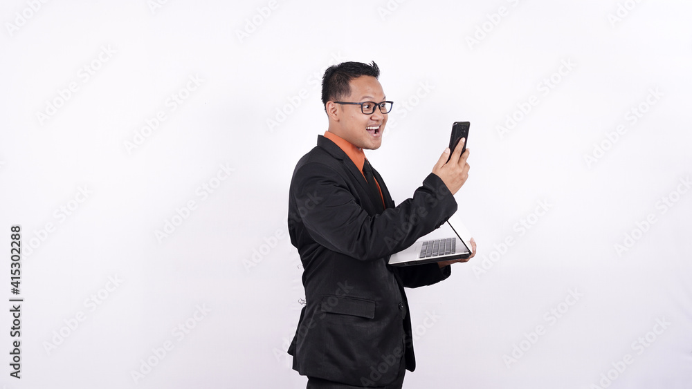 Naklejka premium businessman holds a laptop computer and looks at a cell phone isolated white background