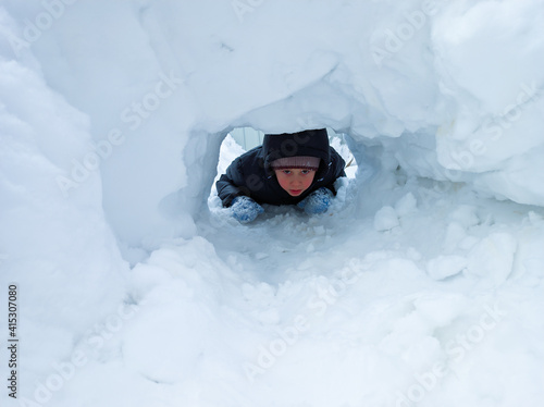 A little boy crawls through a snow tunnel. The concept of winter active recreation.