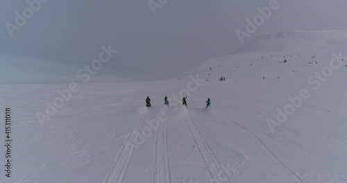 Aerial view: four snow bikers on snowmobiles ride together in a mountain valley. an epic video of a friendly team of snowmobilers riding through a large snow-white canyon high in the mountains at dawn