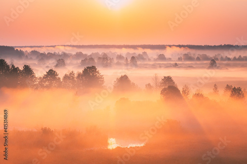 Amazing Sunrise Over Misty Landscape. Scenic View Of Foggy Morning Sky With Rising Sun Above Misty Forest And River. Early Summer Nature Of Eastern Europe. Sunset Dramatic Sunray Light Sunbeam