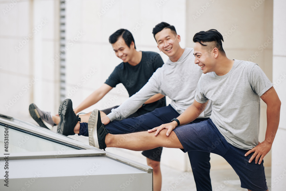 Group of fit young Asian sportsmen stretching legs after jogging outdoors together Group of fit young Asian sportsmen stretching legs after jogging outdoors together