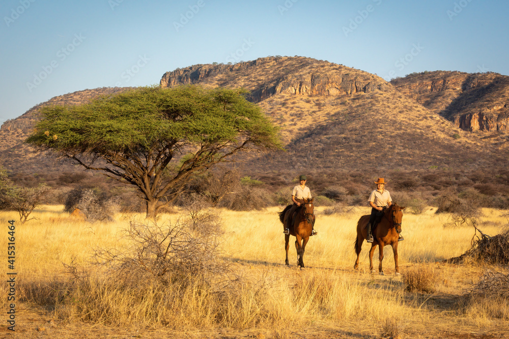 Two women ride past acacia and hills