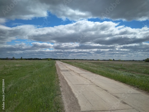 straight road ahead among the green grass in the clouds in the sky in summer travel