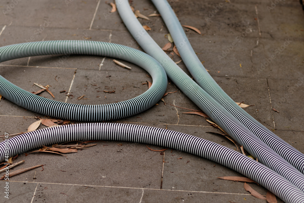 Pool hoses over a tiled outdoor floor with dry leaves
