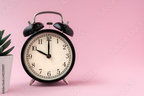 Black vintage alarm clock on a light pink background shows the time ten hours. Copy space.