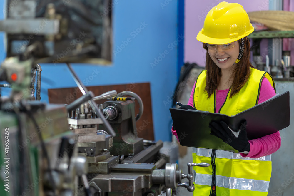 Portrait of Asian woman sales engineer checking the job list in paper over the photo blurred of lathe and milling machine background in metal factory, business industry with safety concept Portrait of Asian woman sales engineer checking the job list in paper over the photo blurred of lathe and milling machine background in metal factory, business industry with safety concept