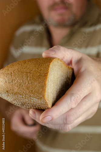 A middle-aged man with a beard and mustache holds out half a loaf of rye bread to the cell.