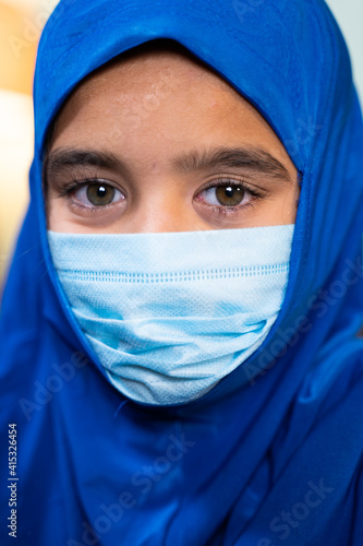 Head shot o Muslim Girl with hijab and medical face mask looking at camera - Concept of coronavirus covid-19 healthcare and protection. photo