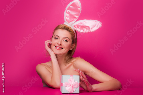 Happy woman with gift box and bunny ears at celebration Easter, isolated on pink.