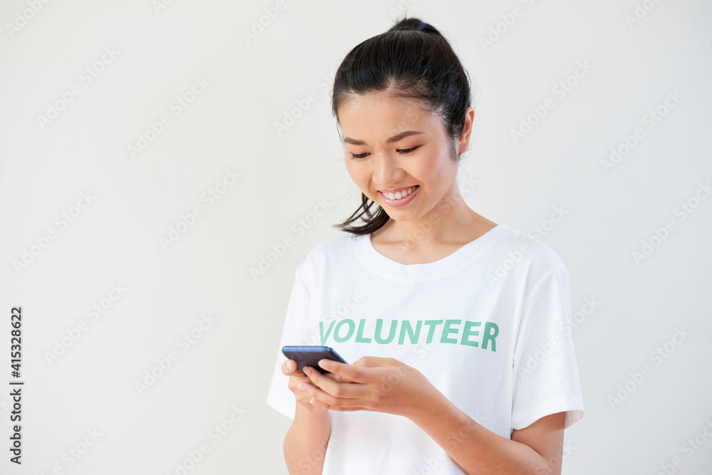 Pertty smiling young woman texting other volunteers from her organization Pertty smiling young woman texting other volunteers from her organization