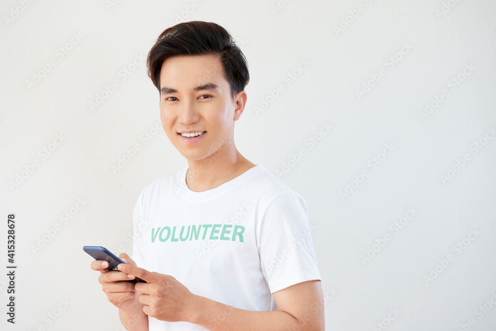 Portrait of handsome young Asian volunteer with smartphone in hands smiling at camera Portrait of handsome young Asian volunteer with smartphone in hands smiling at camera