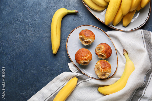 Plate with tasty cupcakes and bananas on dark background
