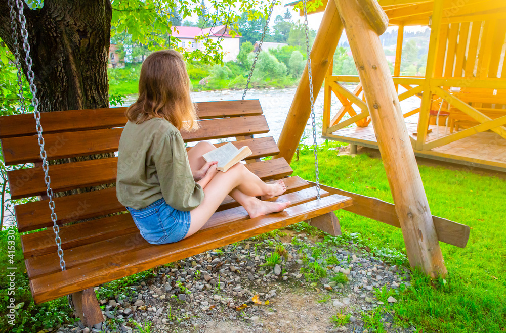 Hipster girl is reading a book on wooden bench. Woman relaxing outdoors on porch swing in the nature. Cozy photo. Summer mood. Hipster girl is reading a book on wooden bench. Woman relaxing outdoors on porch swing in the nature. Cozy photo. Summer mood.