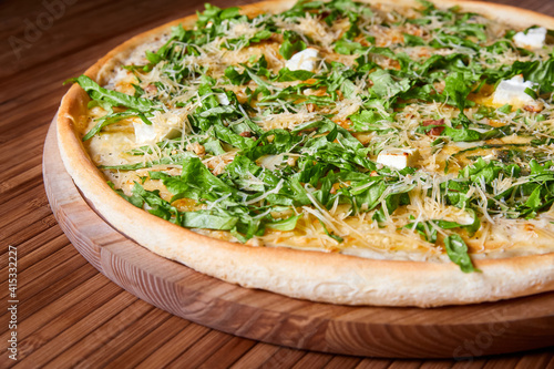 Pizza with cheeses and herbs on a wooden plate. Close-up, selective focus