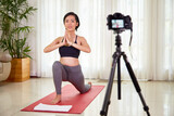 Smiling pretty Vietnamese woman set camera to film herself doing low lounge to increase flexibility in hips