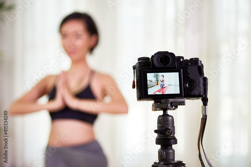 Digital camera filming fit young woman practicing yoga at home, selective focus