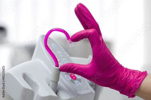Saliva ejector and a hand in a disposable glove symbolize love in dentistry.Hand in a pink glove.Pink saliva ejector.The atmosphere of the dental office.With love in dentistry.Heart symbol.
