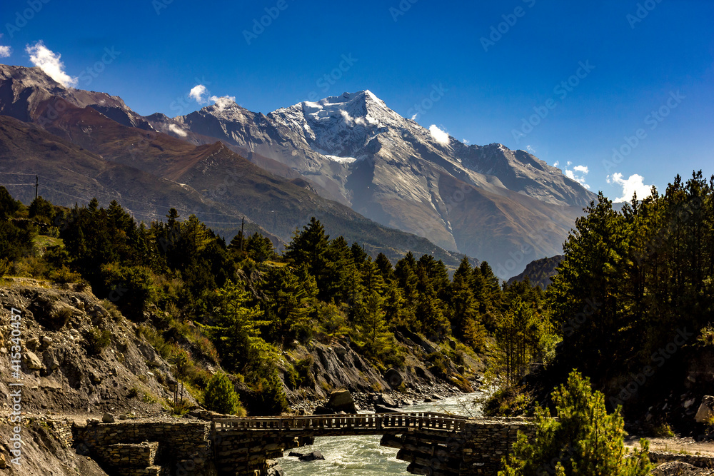 old wooden bridge over marsyandgi river and snowy mount pisang peak in the background in annapurnas of nepal