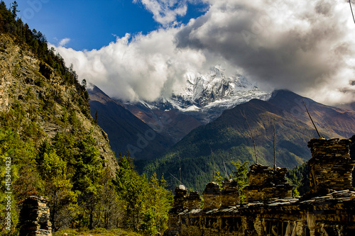 old stone temple in nepal with forest and snowy and cloud covered annapurna in background