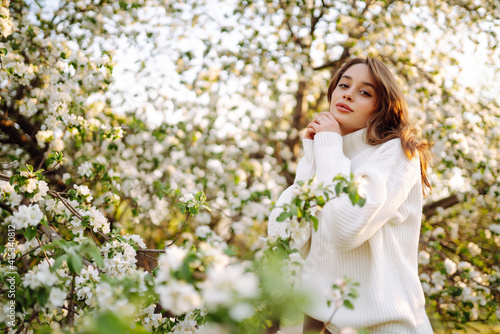 Portrait of Beautiful  Woman In hat  posing near flowering tree. Smiling young woman enjoying smell of flowers on background of spring garden.  Fashion, lifestyle.  © maxbelchenko