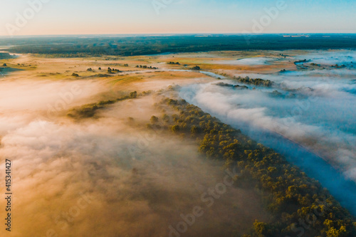 Aerial  view of a beautiful summer  landscape with a fog while dawn.  Photo from drone of a foggy landscape in spring. Top view to land while sunrise. Early morning in nature  misty  weather.