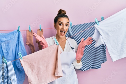 Beautiful brunette young woman washing clothes at clothesline celebrating crazy and amazed for success with arms raised and open eyes screaming excited. winner concept