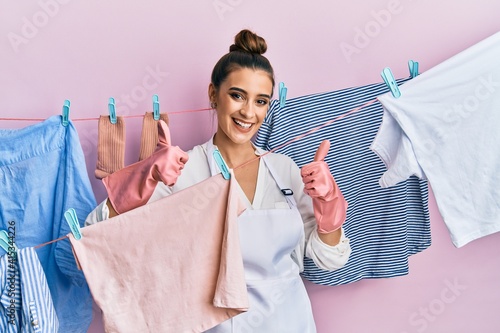 Beautiful brunette young woman washing clothes at clothesline success sign doing positive gesture with hand, thumbs up smiling and happy. cheerful expression and winner gesture.