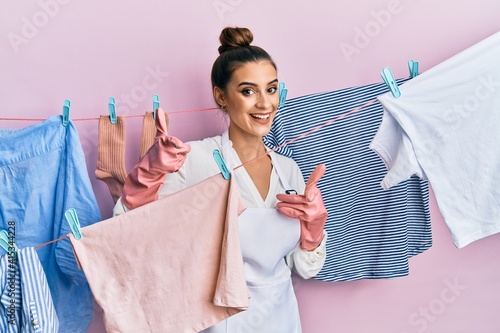 Beautiful brunette young woman washing clothes at clothesline pointing fingers to camera with happy and funny face. good energy and vibes.