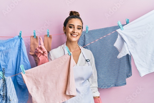 Beautiful brunette young woman washing clothes at clothesline showing and pointing up with finger number one while smiling confident and happy.