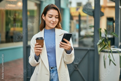 Young hispanic woman using smartphone and drinking coffee at the city.