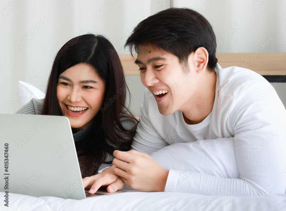 Young Asian black long hair woman and clear face man lovers laying on bed and using notebook computer to serf internet together with relax and happy Young Asian black long hair woman and clear face man lovers laying on bed and using notebook computer to serf internet together with relax and happy
