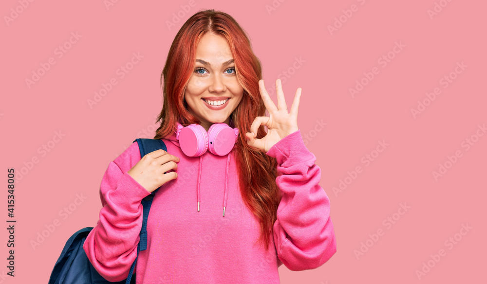 Young redhead woman holding student backpack and books doing ok sign with fingers, smiling friendly gesturing excellent symbol Young redhead woman holding student backpack and books doing ok sign with fingers, smiling friendly gesturing excellent symbol