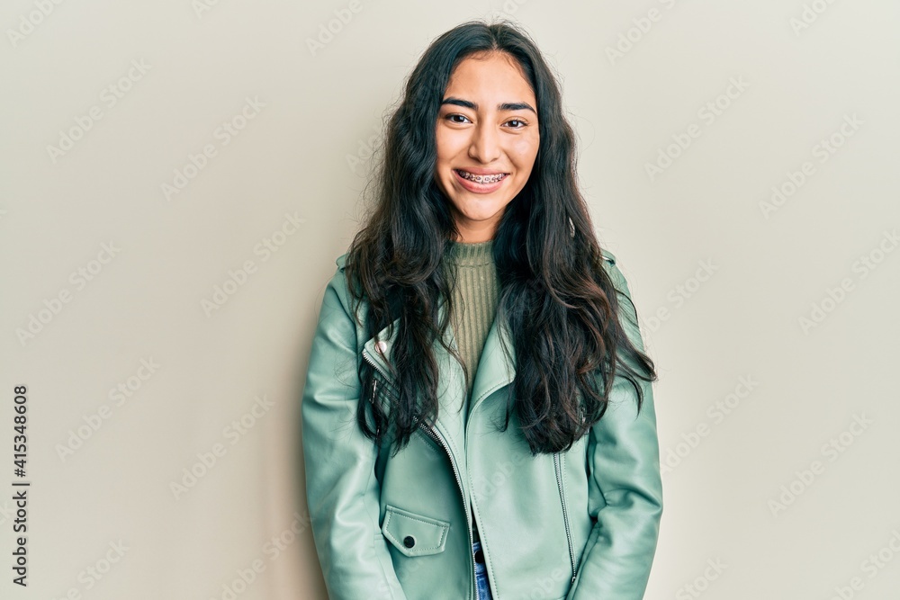 Hispanic teenager girl with dental braces wearing green leather jacket with a happy and cool smile on face. lucky person. Hispanic teenager girl with dental braces wearing green leather jacket with a happy and cool smile on face. lucky person.