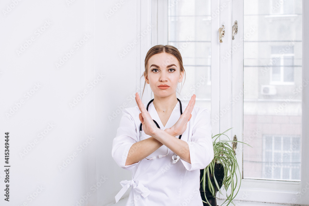 Quarantine bans concept. Doctor woman in a white coat with a stethoscope shows a prohibitory gesture with her hands on the background of a window in a hospital.
Quarantine bans concept. Doctor woman in a white coat with a stethoscope shows a prohibitory gesture with her hands on the background of a window in a hospital.