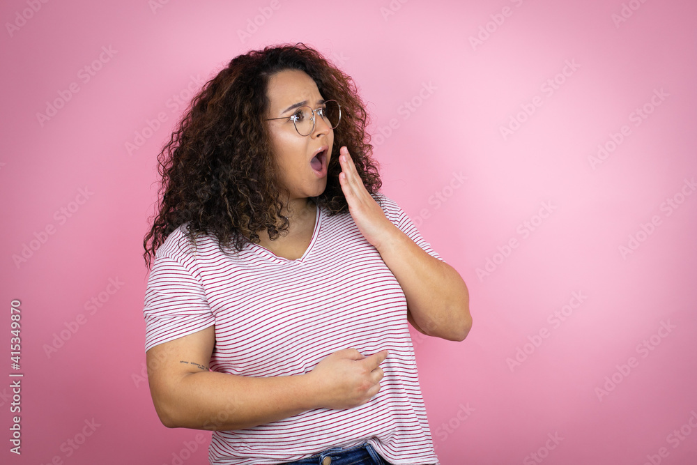 Young african american woman wearing red stripes t-shirt over pink background covering mouth with hand, shocked and afraid for mistake. surprised expression Young african american woman wearing red stripes t-shirt over pink background covering mouth with hand, shocked and afraid for mistake. surprised expression