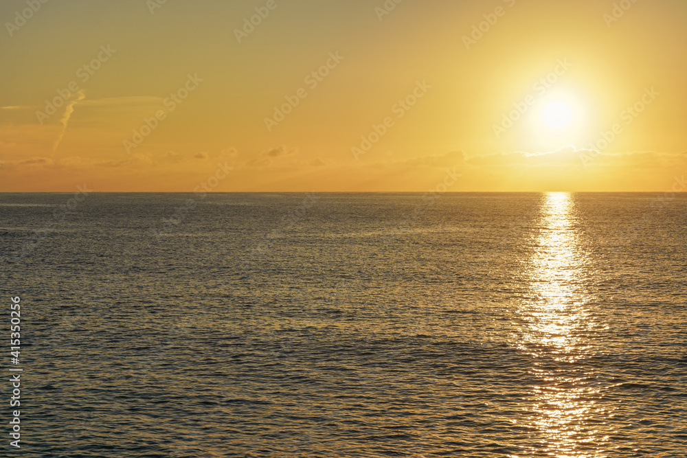 Obraz premium Sun rising above calm sea, clouds coloured to orange