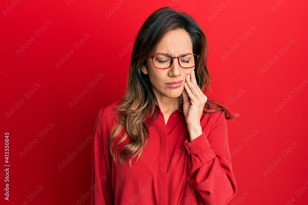 Young latin woman wearing casual clothes and glasses touching mouth with hand with painful expression because of toothache or dental illness on teeth. dentist Young latin woman wearing casual clothes and glasses touching mouth with hand with painful expression because of toothache or dental illness on teeth. dentist