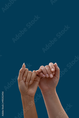 Close up of two hands hooking each other little finger pinkie as a symbol of promise or pardon isolated on blue background