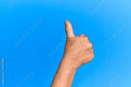 Hand of senior hispanic man over blue isolated background doing successful approval gesture with thumbs up, validation and positive symbol © Krakenimages.com