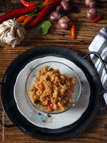 Spicy grated coconut or kelapa bumbu urap which commonly mixed with various steamed vegetables to be urap sayur or Indonesian traditional salad. Served in clear bowl on wooden table with ingredients.  photo