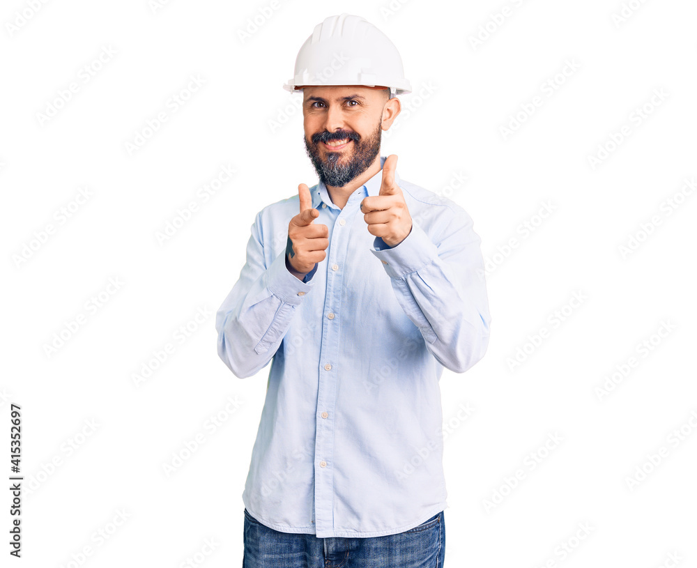 Young handsome man wearing architect hardhat pointing fingers to camera with happy and funny face. good energy and vibes. Young handsome man wearing architect hardhat pointing fingers to camera with happy and funny face. good energy and vibes.