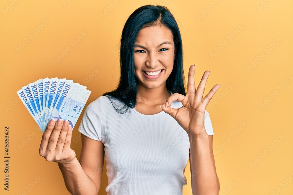 Beautiful hispanic woman holding 1000 south korean won banknotes doing ok sign with fingers, smiling friendly gesturing excellent symbol Beautiful hispanic woman holding 1000 south korean won banknotes doing ok sign with fingers, smiling friendly gesturing excellent symbol