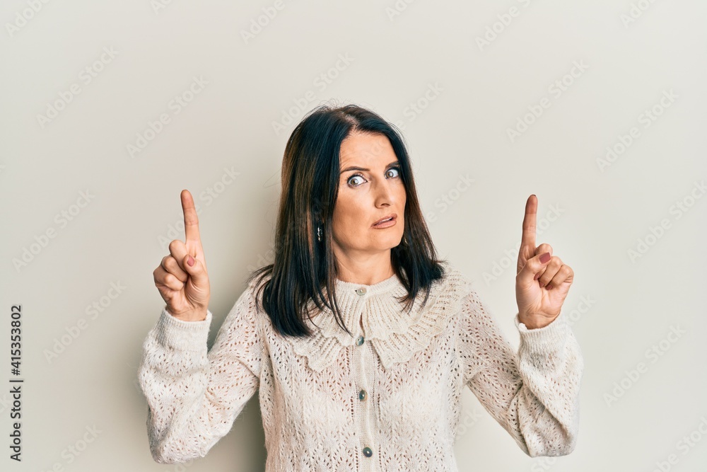 Middle age brunette woman pointing up with fingers clueless and confused expression. doubt concept. Middle age brunette woman pointing up with fingers clueless and confused expression. doubt concept.