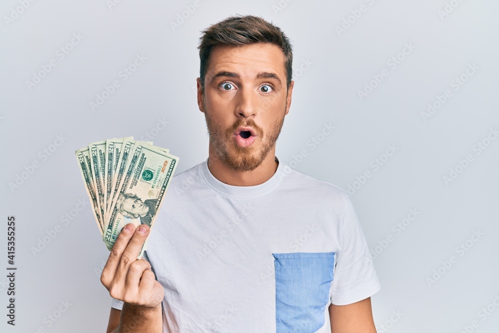 Handsome caucasian man holding 20 dollars banknote scared and amazed with open mouth for surprise, disbelief face Handsome caucasian man holding 20 dollars banknote scared and amazed with open mouth for surprise, disbelief face