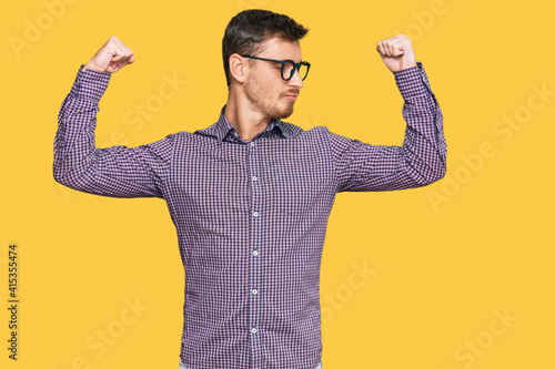 Handsome caucasian man wearing casual clothes and glasses showing arms muscles smiling proud. fitness concept.
