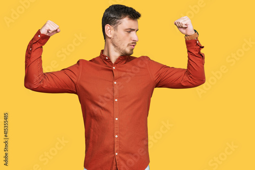Handsome caucasian man wearing casual clothes showing arms muscles smiling proud. fitness concept.