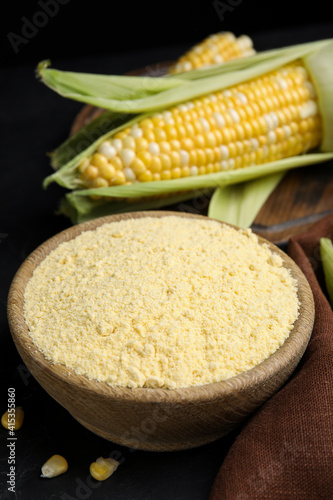 Corn flour in bowl and fresh cobs on black table